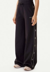 Zwarte sweatpants met wijde pijpen, een elastische tailleband, trekkoorddetails en decoratieve zijstrepen met metalen accenten en logo borduursels.