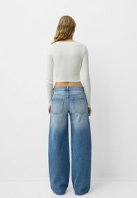 Top cropt cu mânecă lungă albă, asortat cu blugi din denim bleu deschis cu picioare largi, având o spălare ușor decolorată și două buzunare la spate.