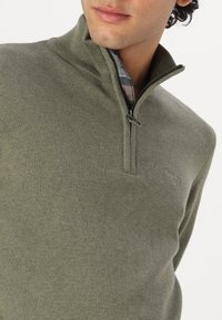 Olivgrüner Reißverschluss-Pullover mit strukturiertem Finish, klassischem Kragen und dezentem Logo auf der Brust. Weicher Stoff, lässiges Design.