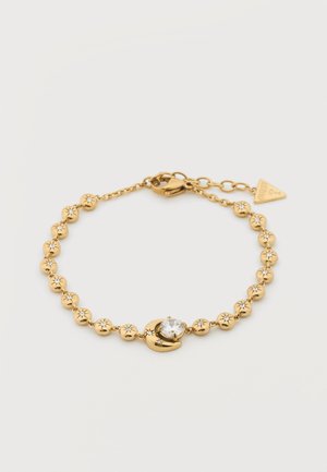 Armband van goudkleurige ketting met kleine kralen gegraveerd met sterren, een maantje-bedel met een ronde heldere edelsteen, en een karabijnsluiting met label.