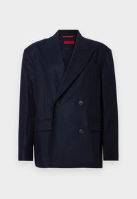 Marineblaues Doppelreiher-Jackett aus glattem Stoff mit geschliffenem Revers, zwei Vordertaschen und schwarzen Knöpfen. Rotes Etikett im Kragen.