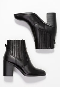 Bottines noires en cuir lisse, dotées d'un talon empilé, de panneaux latéraux élastiques avec nervures verticales et d'un détail de languette de tirage.