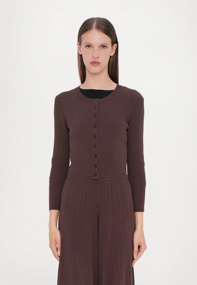 Cardigan marrone a costine con maniche lunghe, scollatura rotonda e chiusura con bottoni frontali. Tessuto liscio, design aderente, indossato sopra un top nero.