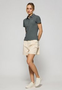 Grå pikétröja med krage, beige cargoshorts och vita sneakers. Enkel design, mjuk kvalitet och sidoflik på tröjan.