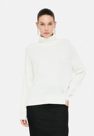 Maglione bianco a collo alto lavorato a maglia con polsini a costine, con un logo a forma di cuore di un beige chiaro all'orlo. Abbinato a una gonna nera.