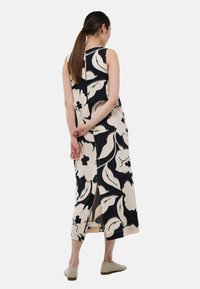 Robe maxi à motifs floraux en noir et beige, avec un design sans manches et des fentes sur les côtés. Associée à des chaussures beige à enfilement.