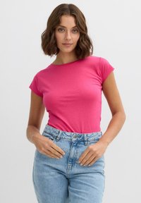 Camiseta de algodón ajustada de color rosa, con mangas cortas y cuello redondo, combinada con unos vaqueros de tiro alto de color azul claro. Textura suave.
