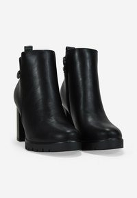 Par de botines de cuero negro con tacones de bloque, cremalleras laterales y lengüetas de tirón sobre un fondo blanco.