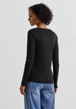 Maglietta nera a maniche lunghe con scollatura rotonda, realizzata in tessuto morbido, abbinata a jeans a gamba larga in denim blu con tasche posteriori.