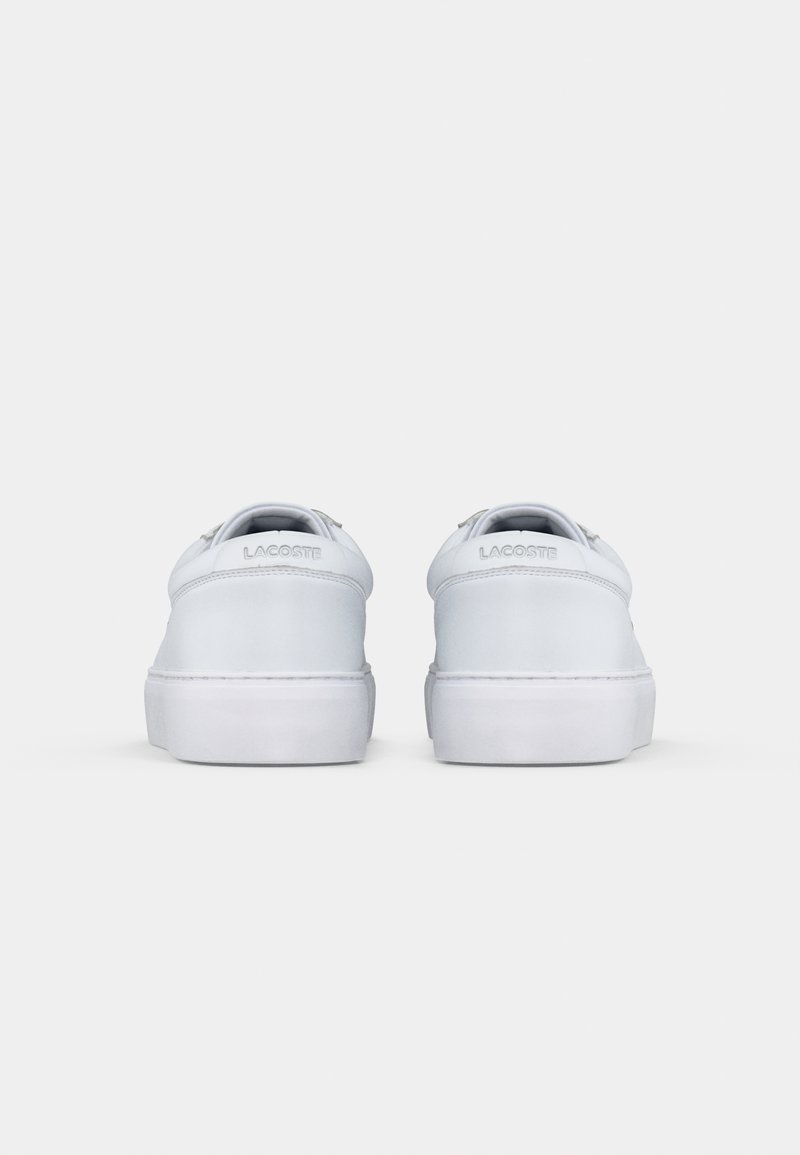 White leather sneakers with a smooth finish, flat rubber soles, and embossed logo on the heel. Simple, rounded design with minimal accents.