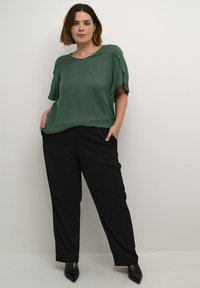 Grøn, struktureret kortærmet top parret med sorte, løstsiddende bukser. Outfittet har et simpelt design og er komplementeret af spidse sorte sko.