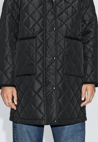 Gestepptes schwarzes Jackett mit Druckknopfverschlüssen, zwei Fronttaschen und gerippten Bündchen, aus einem glatten, leichten Stoff gefertigt.