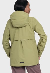 Hellgrüne wasserdichte Jacke mit Kapuze, elastischen Bündchen und einem Rückenschlitz für Belüftung. Mit einem schwarzen Logo-Detail in der Nähe des Saums.