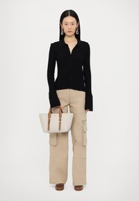 Cămășă neagră cu dungi și nasturi, pantaloni cargo bej cu buzunare, geantă cu model crem și mânere maronii, și pantofi cu platformă maronii.