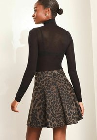 Schwarzes Langarmoberteil kombiniert mit einem Rock im Leopardenmuster. Der Rock hat ein ausgestelltes Design und zeigt braune und schwarze Farbtöne mit einer glatten Textur.