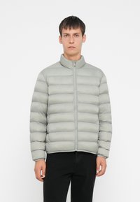 Lys grå pufferjakke med stående krage, glidelås foran og horisontal quiltet design. Stoffet virker glatt og polstret.