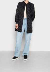 Chaqueta bomber negra acolchada con cremallera frontal y puños de canalé, combinada con pantalones de mezclilla azul claro y zapatillas negras.