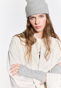 Szürke bordázott sapka, bézs csíkos póló, és szürke ujjatlan kesztyű. Puha textúrák, laza fazon, réteges kialakítás és kontrasztos színek.