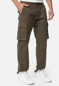 Olive cargo pants with multiple side pockets, made of sturdy cotton material. Features a relaxed fit and reinforced stitching. Paired with white sneakers.