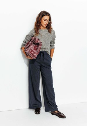 Pull gris côtelé avec boutons, pantalon large à carreaux bleu marine, et sac à motifs bordeaux, complété par des mocassins foncés.