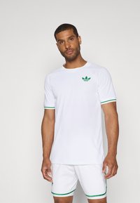 Valge sportlik T-särk roheliste detailidega varrukate otstes, vasakul rinnal rohelise logoga. Kerge ja hingav materjal.