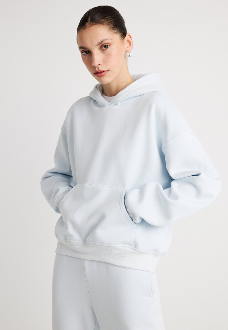 Sweatshirt azul-claro oversized feito de tecido macio, com um bolso frontal, punhos canelados e um capuz aconchegante. Combinado com calças a condizer.