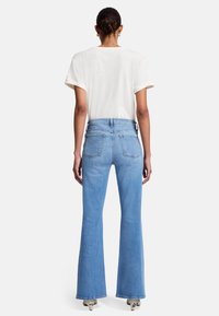 Jeans a zampa d'elefante blu chiaro con vita alta, cinque tasche e orlo risvoltato. Abbinati a una t-shirt bianca a maniche corte.