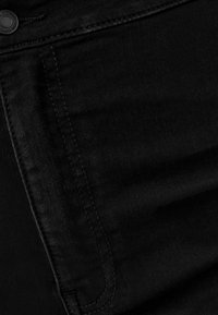 Mustat farkut, joissa on sileä pinta, klassinen viiden taskun muotoilu ja sävyyn sointuva ompelu reunojen ympärillä virtaviivaisen ilmeen saavuttamiseksi.