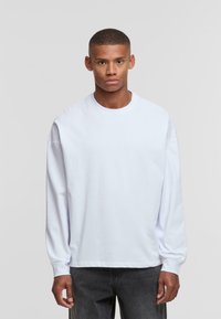 White long-sleeve T-shirt with a round neck, made of a smooth cotton fabric. Loose fit and ribbed cuffs, paired with dark gray jeans.