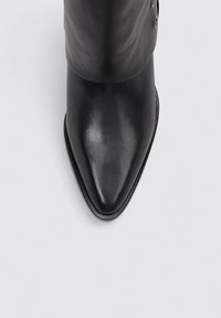 Bota de piel negra con Punta afilada y acabado suave, con un caña alta que presenta acentos de botones en el lateral y una suela delgada.