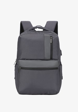 Un sac à dos gris avec des bretelles rembourrées, plusieurs compartiments zippés et une poignée de transport en haut sur un fond blanc.