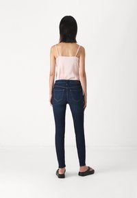 Mörkblå, figursydda jeans med bakfickor och en slät finish. Kombineras med en ljusrosa linne och svarta sandaler.