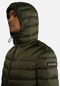 Giacca imbottita verde oliva con cappuccio, dotata di chiusura a zip, texture imbottita e patch con logo sulla manica.