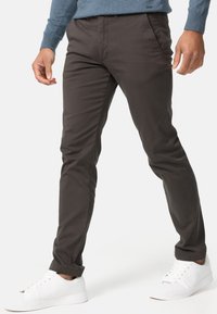 Mörkbruna slim-fit byxor i slät tyg, med fickor och upprullade ärmslut, ihop med vita sportskor.