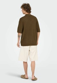 Knit brown short-sleeve top with a relaxed fit, paired with light beige knee-length shorts and brown slip-on sandals.