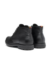 Botas de tobillo de cuero negro con superficie texturizada, parte delantera con cordones y suela robusta. Presenta una etiqueta colorida en el talón.
