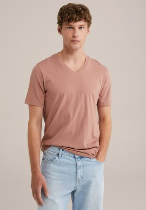 V-Ausschnitt, kurzärmeliges T-Shirt in einer staubigen Rosa-Farbe, aus einem glatten Stoff gefertigt. Getragen mit hellblauen Jeans, die einen lockeren Schnitt zeigen.