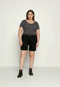 Shorts de ganga preta com fecho frontal por botão, combinados com uma t-shirt ajustada de mangas curtas cinza e botas pretas até ao tornozelo. Textura suave.