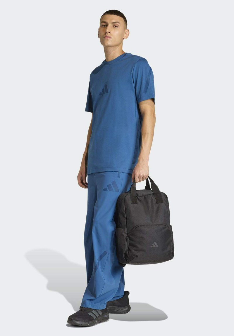 Maglietta atletica blu con logo scuro, pantaloni blu abbinati, zaino nero con logo e scarpe nere. Design semplice, stile sportivo casual.