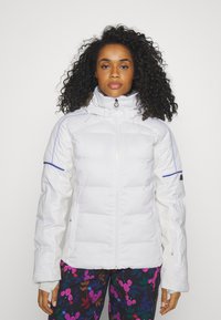 Weißer isolierter Jacke mit hohem Kragen, Reißverschluss und blauen Akzenten, kombiniert mit floral gemusterten Hosen.
