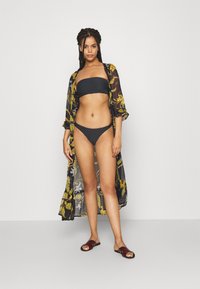 Melns bandeau stila bikini ar atbilstošām biksēm, kopā ar caurspīdīgu, ziedu raksta gariem kimoniem melnā, dzeltenā un pelēkā krāsā. Brūni slaidi čības.