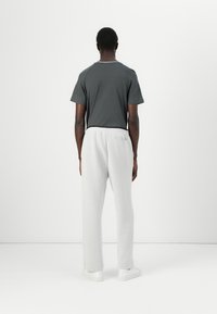 Dark gray short-sleeve t-shirt with a textured back panel, paired with light gray joggers and white sneakers, viewed from the back.