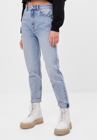 Ljust blå denimjeans med hög midja, raka ben och uppvikta ärmar, tillsammans med vita snörkängor med en tjock, texturerad sula.
