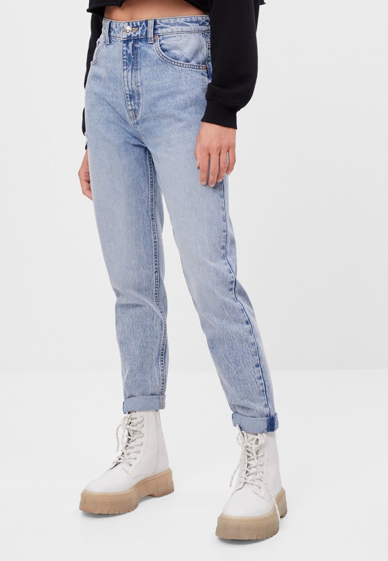 Ljust blå denimjeans med hög midja, raka ben och uppvikta ärmar, tillsammans med vita snörkängor med en tjock, texturerad sula.
