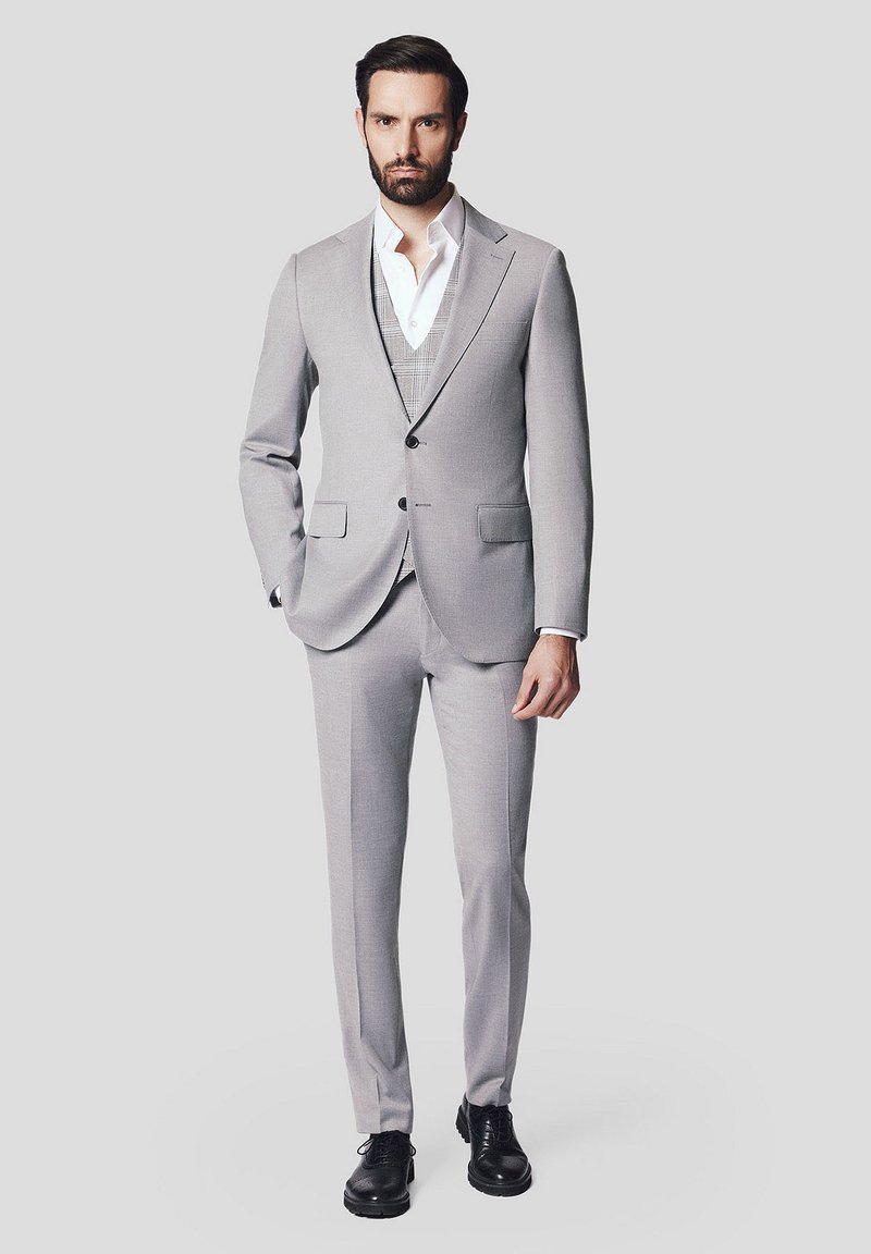Jasnoszary garnitur z dopasowaną marynarką, pasującymi spodniami i kamizelką w kratę. Stylistycznie połączony z białą koszulą i czarnymi butami. Gładka tekstura.