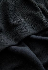 Close-up of black textured fabric with fine ribbing, intricate stitching, and the word "NEXT" subtly embroidered.