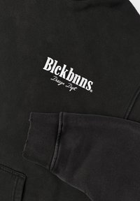 Zwarte sweatshirt van een katoenmix, met een witte geborduurde logo "Blckbnns Design Dept" op de linkerborst en geribde mouwen.