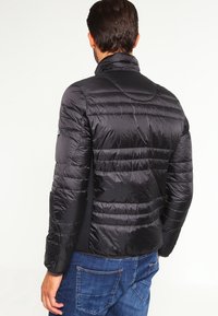 Svart puffjacka med hög krage och horisontell sömnad. Slätt, lätt material med en åtsittande design, tillsammans med blå denimjeans.