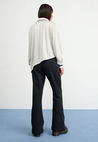 Világosszürke, hosszúujjú dzseki ívelt hemel, sötét tengerészkék díszítéssel a mandzsettákon, fekete, bő szabású nadrággal és masszív fekete csizmával párosítva.