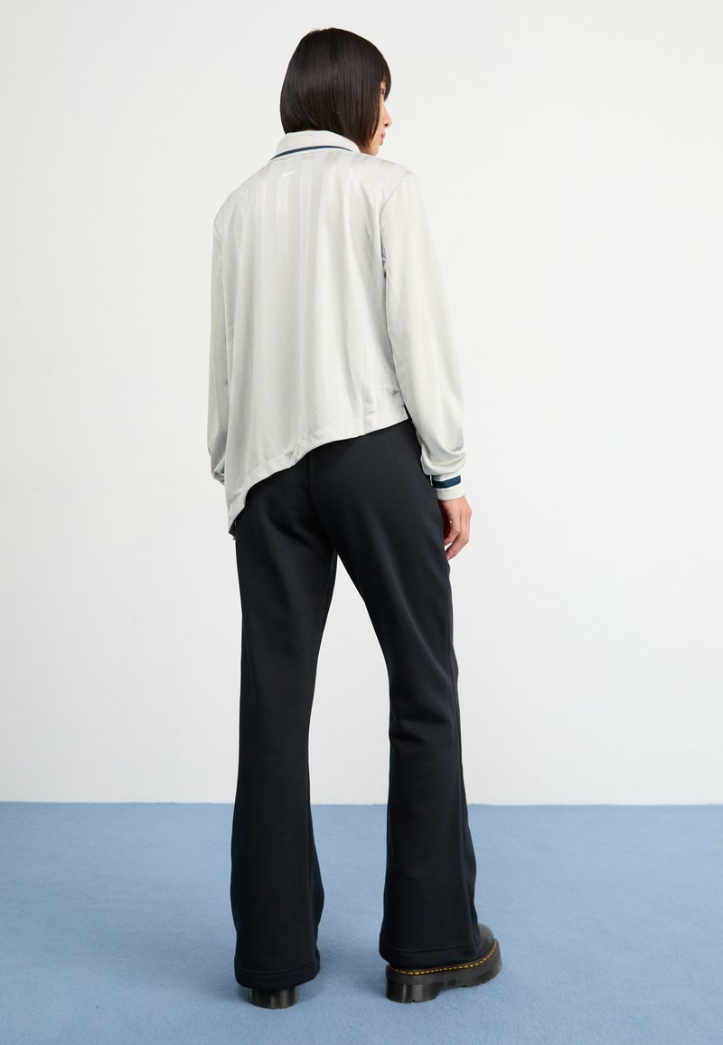 Veste gris clair à manches longues avec un ourlet incurvé, accents bleu marine foncé sur les poignets, associée à un pantalon noir évasé et des bottes noires chunky.